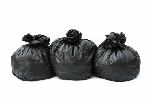 Three black plastic rubbish bags, tightly tied at the top, are arranged in a row against a plain white background. The bags appear to be full, with a slightly shiny surface and some folds and creases visible on their texture. They are positioned in a way that suggests they may have been gathered for disposal, typical of rubbish removal services in Willesden. The simple presentation emphasizes the compactness and uniform size of the bags, which are commonly used in garden clearance and general waste collection. This image reflects the type of waste packaging handled by Garden Clearance Willesden, illustrating the process of preparing rubbish for collection and removal from residential or commercial properties in north-west London. The clean background highlights the bags clearly, making the visual suitable for online content related to domestic rubbish clearance services.